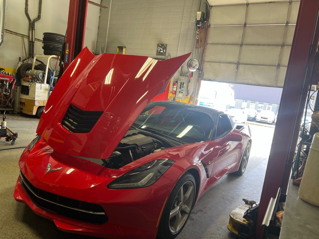 Red C7 Chevrolet Corvette with its hood open in the AMR Automotive workshop